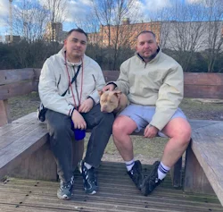 two men sitting on a bench with a dog